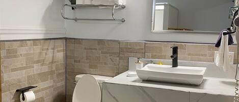 A bathroom with a toilet, sink, mirror, towel rack, and a trash bin.