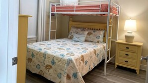 A bunk bed with a patterned bedspread, a bedside lamp, and a small wooden nightstand. - Beach View ● Walks to Sand ● Pools & Hot Tub (Gulf Shores)