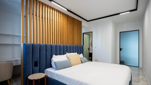 A modern bedroom with a large bed, a wooden slatted headboard, a small stool, and a door. - Coastal Elegance, Steps from the Sea (Sliema)