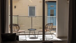 A balcony with two wicker chairs and a small round table, overlooking a building with blue doors and beige walls. - Coastal Elegance, Steps from the Sea (Sliema)