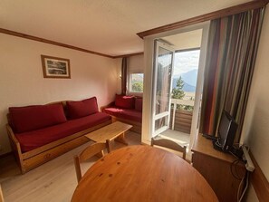 A cozy room with a wooden sofa, a small table, and a view of mountains through a sliding door. - 300m from ski lifts, 1st floor, balcony, tv, ski locker, 28m², Alpe d'Huez (L'Alpe d'Huez)