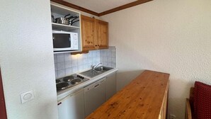 A compact kitchen with white cabinets, a microwave, a sink, and a wooden countertop. - 300m from ski lifts, 1st floor, balcony, tv, ski locker, 28m², Alpe d'Huez (L'Alpe d'Huez)