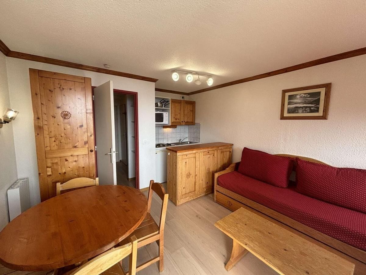 Un espace de vie compact comprenant une table à manger en bois, un canapé rouge et un coin cuisine.