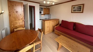 A compact living space with a wooden dining table, a red sofa, and a kitchenette. - 300m from ski lifts, 1st floor, balcony, tv, ski locker, 28m², Alpe d'Huez (L'Alpe d'Huez)