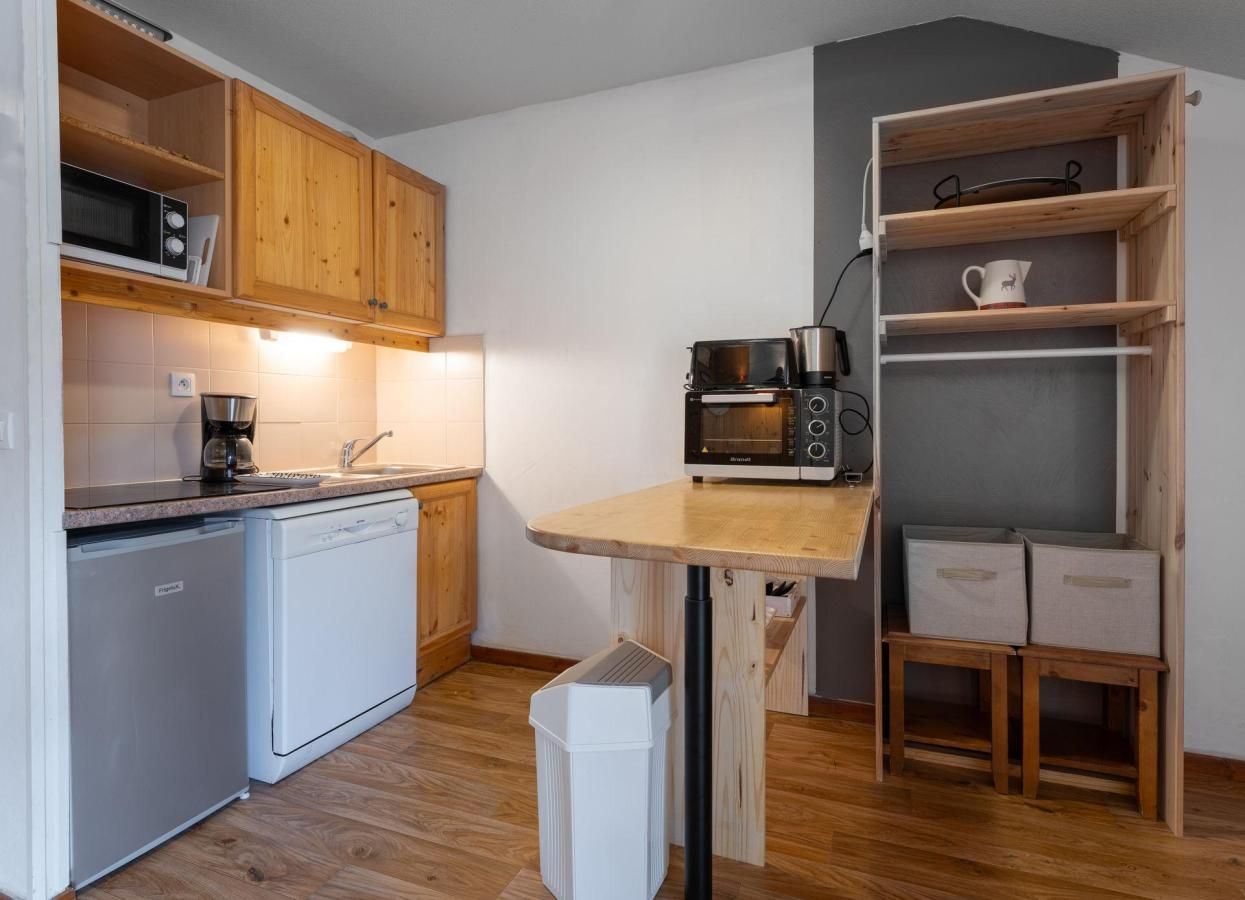 A compact kitchen with wooden cabinets, a microwave, a coffee maker, and a small trash bin.