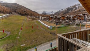 A mountain resort with chalet-style buildings, a ski lift, and a view of snow-capped mountains.