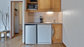 A compact kitchen with wooden cabinets, a microwave, a coffee maker, and a dishwasher.