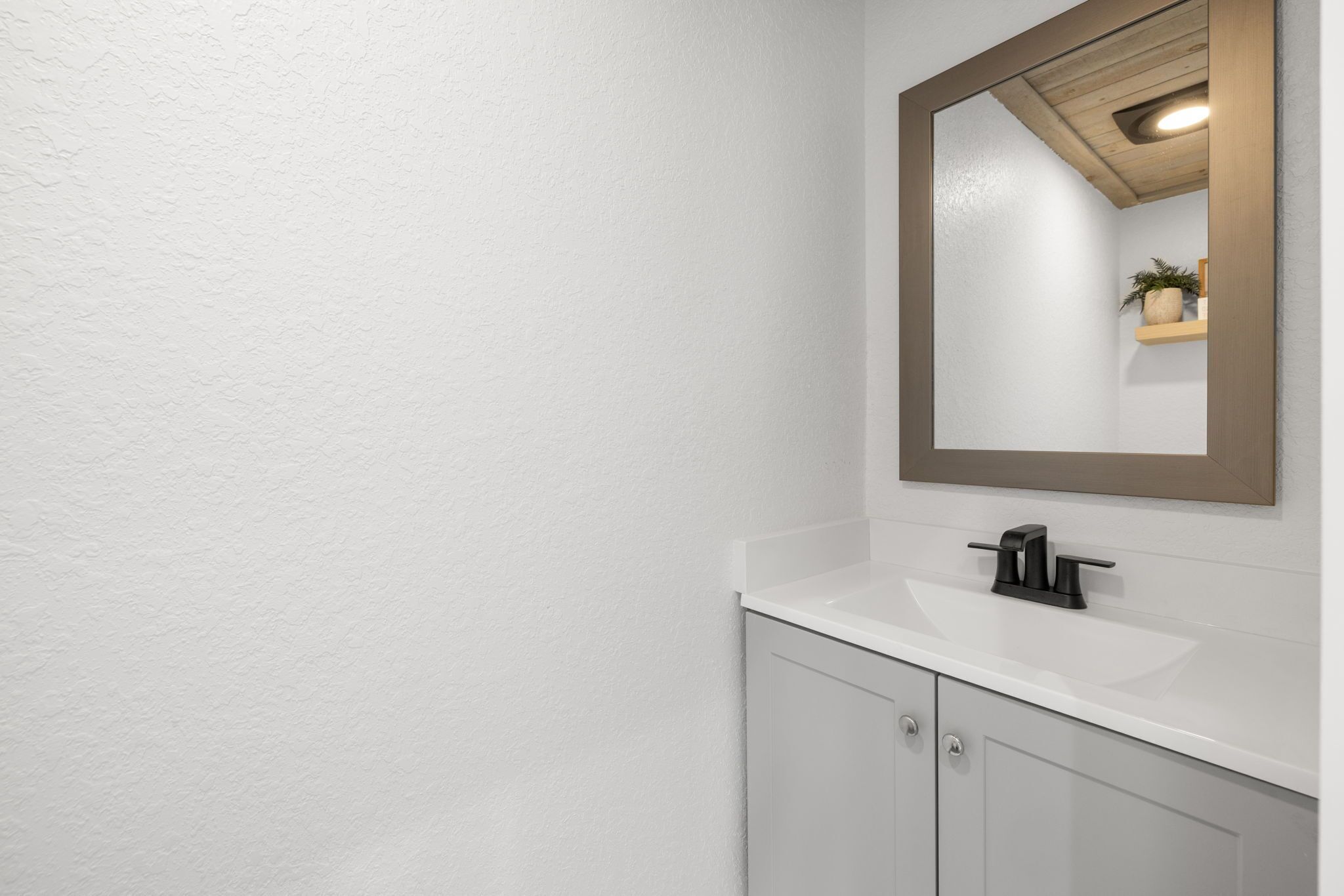 A bathroom with a white sink, a mirror with a wooden frame, and a small shelf with a plant.
