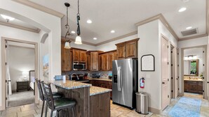 A kitchen with wooden cabinets, a stainless steel refrigerator, and a granite countertop island with bar stools. - The Overlook at Coral Springs (Hurricane)