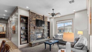 A living room with a stone fireplace, a ceiling fan, and a sofa with a lamp. - The Overlook at Coral Springs (Hurricane)