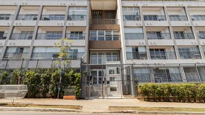 A multi-story residential building with balconies, a gated entrance, and a small garden area.