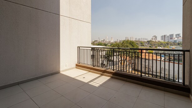 A balcony with a view of a cityscape, featuring a tiled floor and a metal railing.