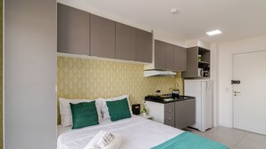 A hotel room with a bed, a kitchenette, and a door.