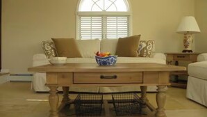 A bedroom with a bed, a wooden nightstand, a lamp, a window with blinds, and a decorative bowl on the nightstand.