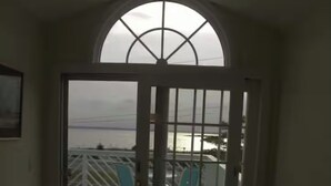A room with a large arched window, a door leading to a balcony, and two chairs.