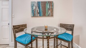 A dining area with a glass table and two chairs with blue cushions, a painting on the wall, and a white door. - Vibrant Memphis Retreat | Steps from Local Spots (Memphis)