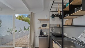 Una cocina moderna con horno empotrado, microondas y fregadero, estanterías de madera y una puerta corrediza de vidrio que da a un área exterior.