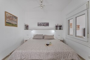 Une chambre à coucher avec un lit, un ventilateur de plafond, des tables de chevet et des œuvres d’art accrochées aux murs.