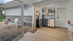 Una cocina moderna con encimera negra, armarios blancos y una pequeña isla. Hay un comedor con una mesa y sillas blancas, además de un balcón con una silla y una mesita.