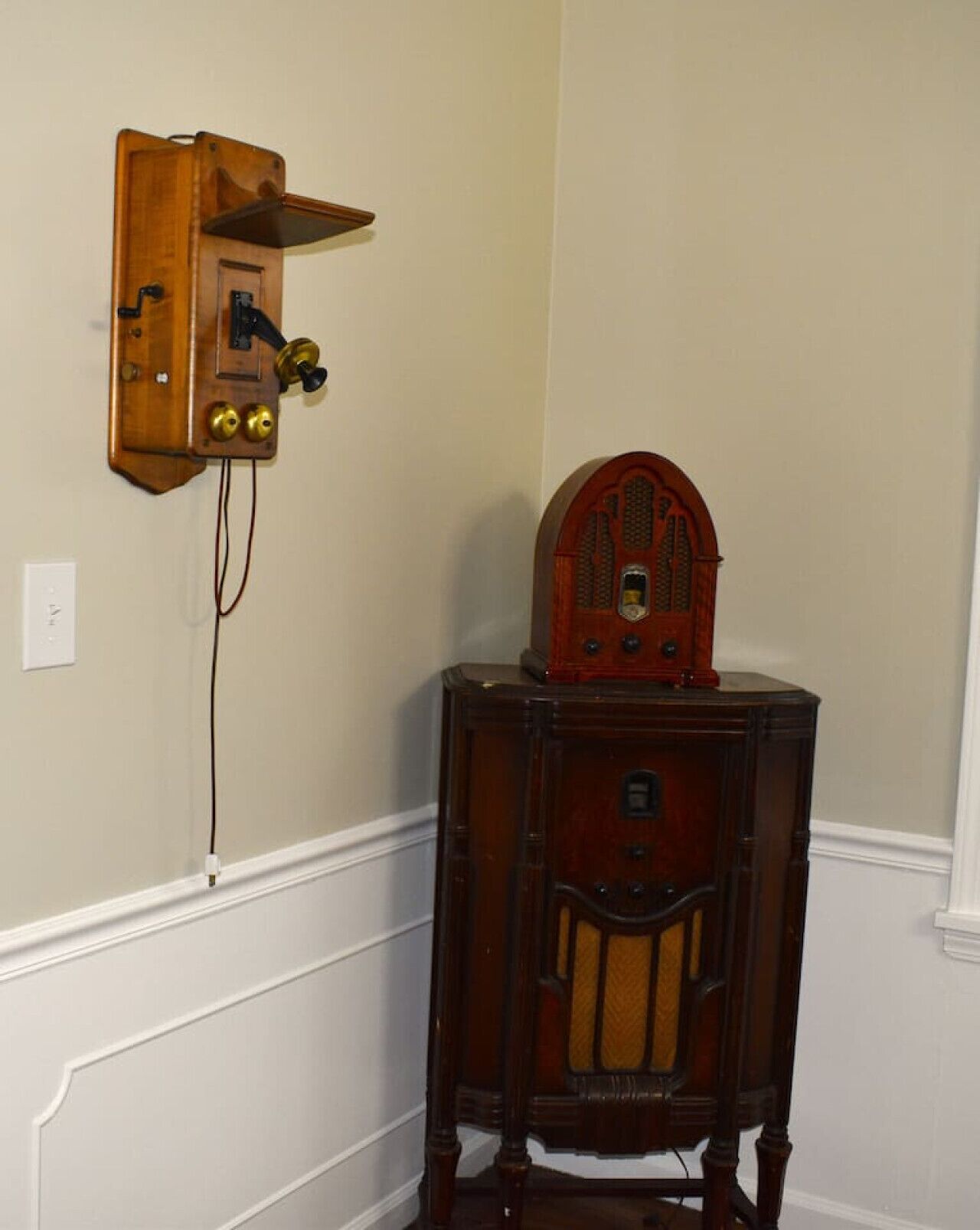 A corner room with a wooden wall-mounted radio and a wooden cabinet with a cushioned chair.