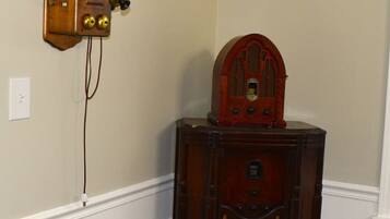 A corner room with a wooden wall-mounted radio and a wooden cabinet with a cushioned chair.