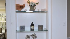 A white interior with a glass shelf unit displaying decorative items. - The House Hotels - Acadia Farms (Northfield)