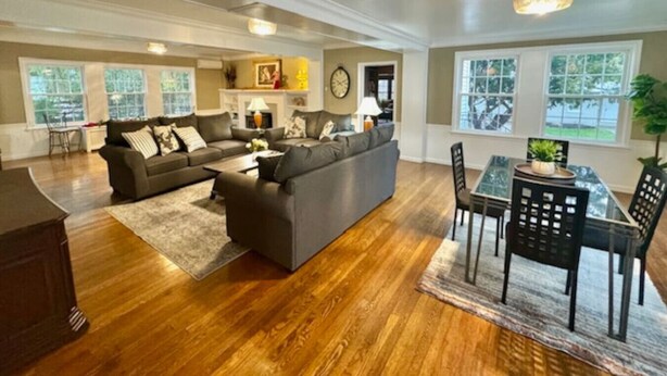 A spacious living room with a large sectional sofa, a dining table with chairs, and a chandelier. - The House Hotels - Acadia Farms (Northfield)