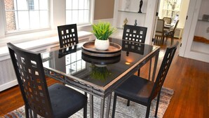 A dining area with a glass table, black chairs, a central plant, and a patterned rug. - The House Hotels - Acadia Farms (Northfield)