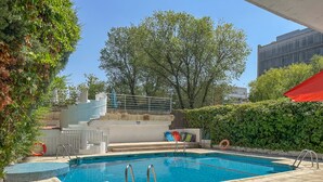 Una piscina con escalones de acceso, rodeada de vegetación y un edificio al fondo.