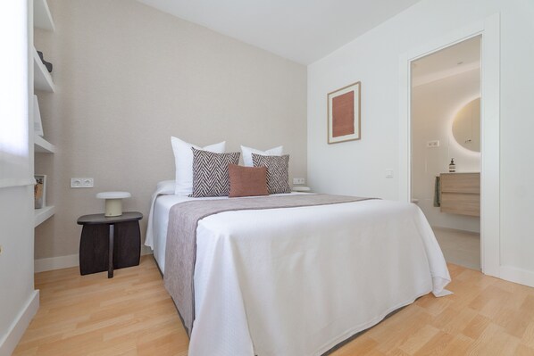 A modern bedroom with a large bed, bedside tables, a mirror, and a small side table.