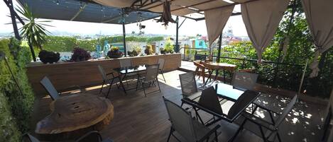 An outdoor patio with a wooden table and chairs, a round wooden table, and a view of the cityscape.