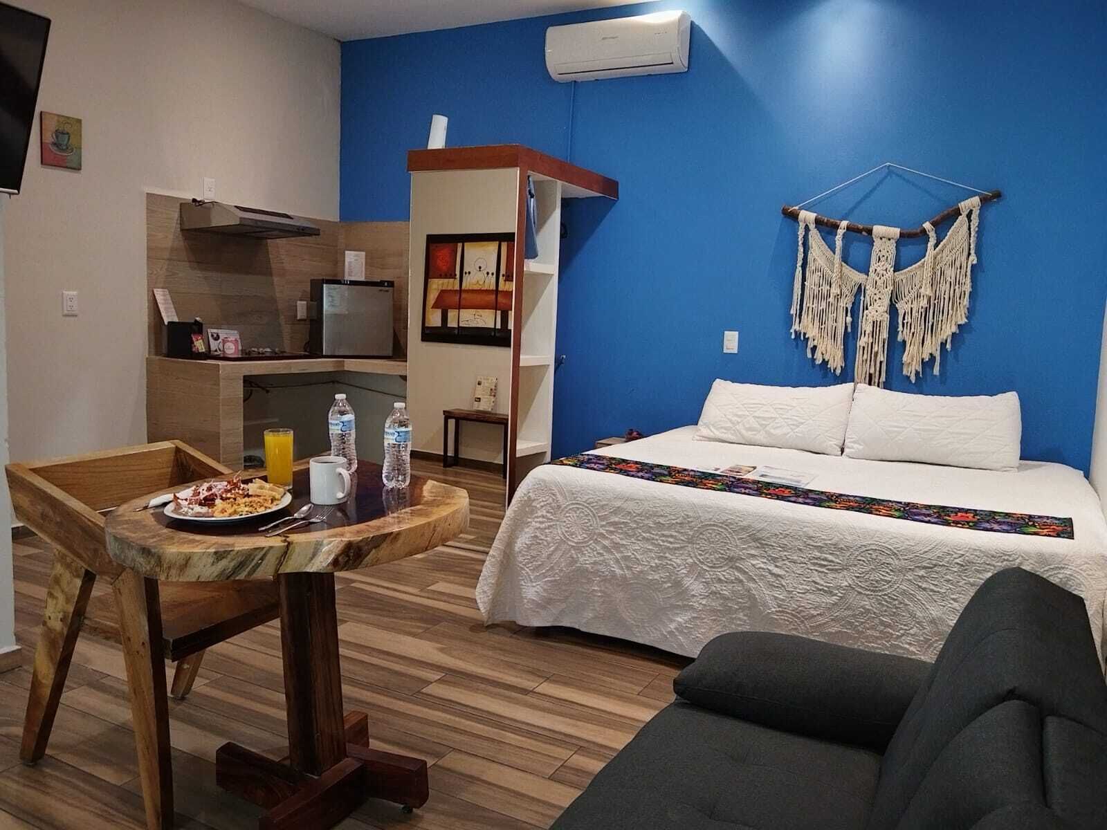 A room with a bed, a table with breakfast, a chair, a macrame wall hanging, and a built-in shelf.