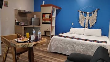 A room with a bed, a table with breakfast, a chair, a macrame wall hanging, and a built-in shelf.