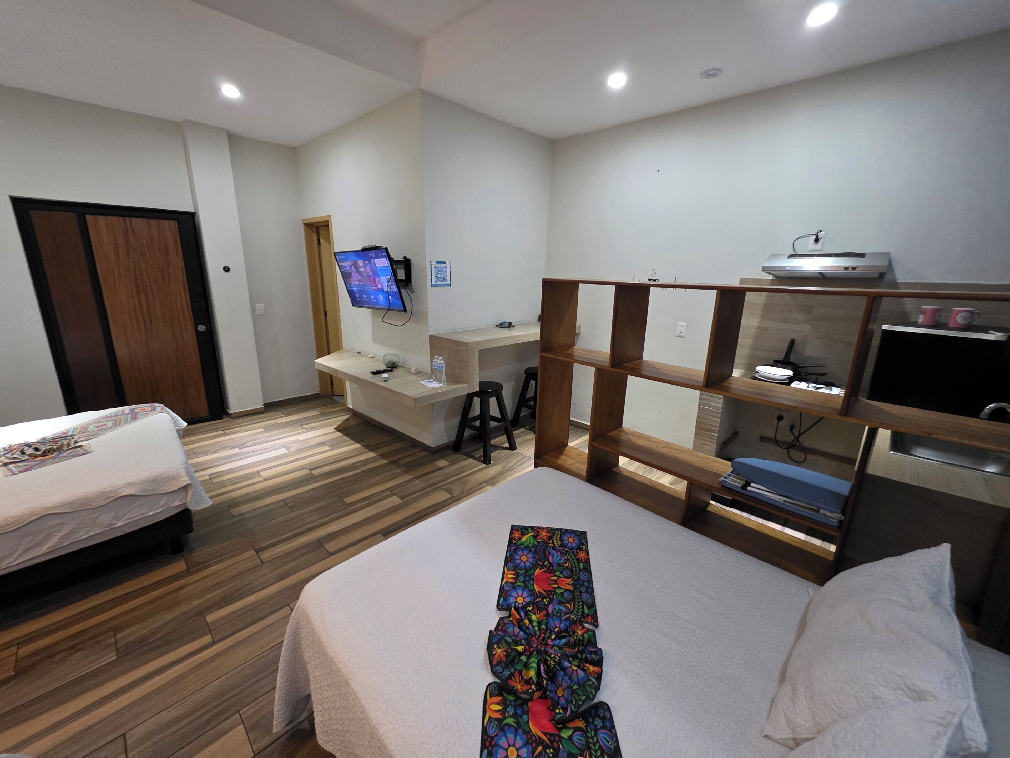 Une chambre d’hôtel avec deux lits, un bureau avec un ordinateur, une télévision et une étagère en bois avec des tasses.