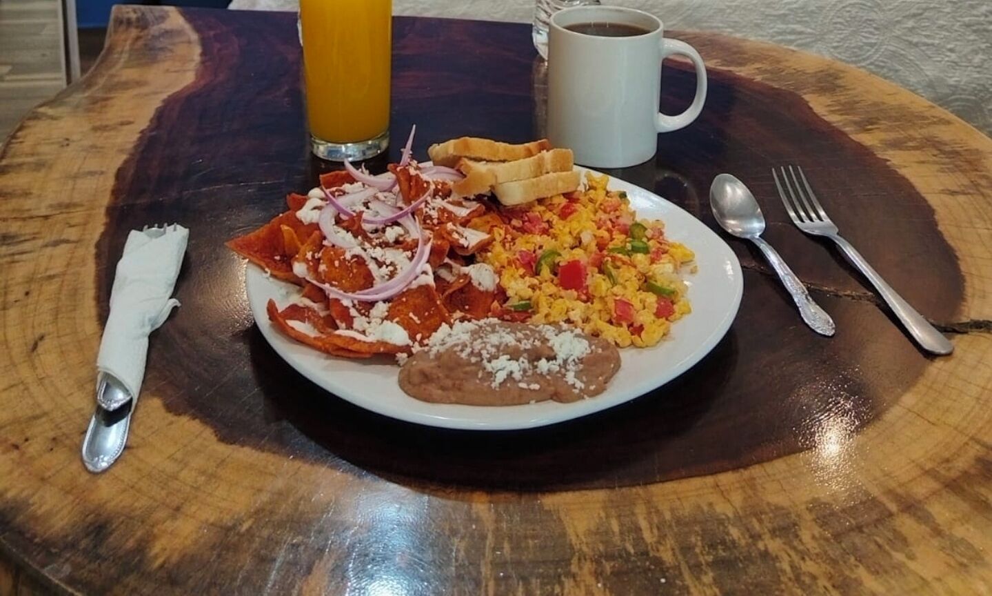 Un plato de desayuno con tostadas, huevos revueltos, frijoles y cebollas rojas sobre una mesa de madera.