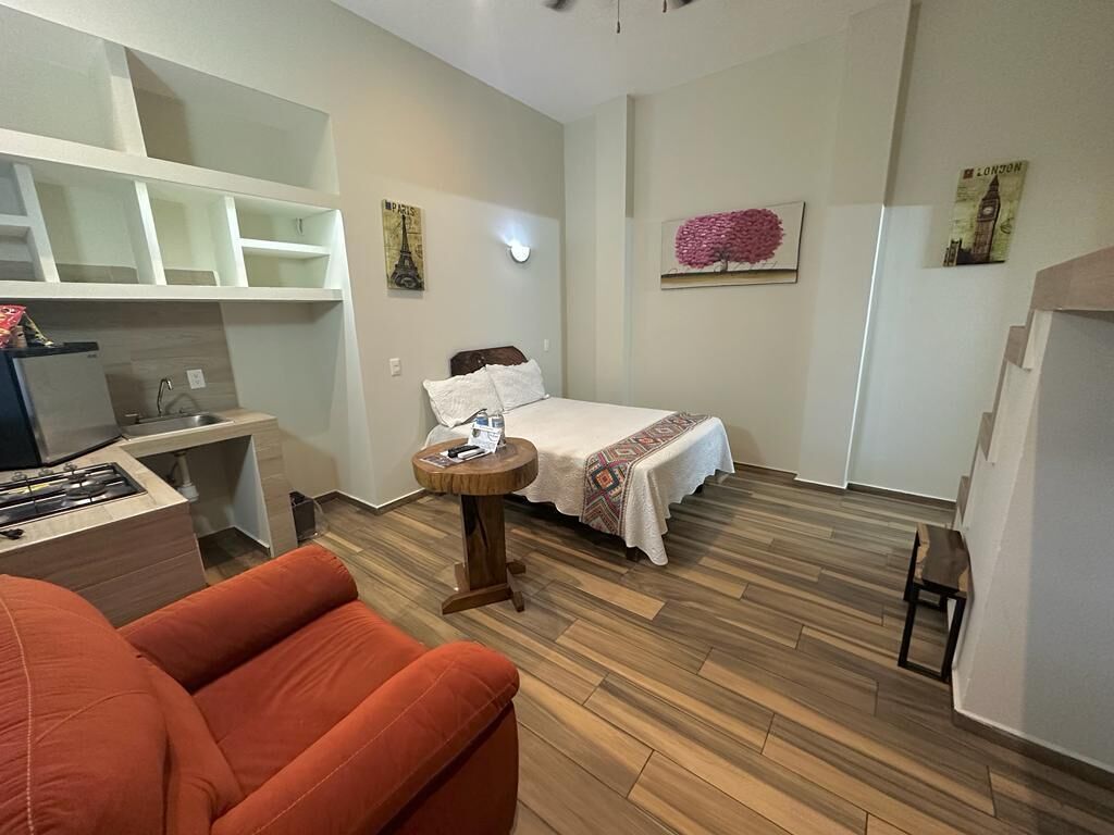 A compact room with a bed, a small round table, a sofa, and a kitchenette area.