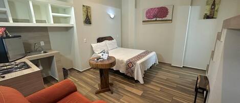 A compact room with a bed, a small round table, a sofa, and a kitchenette area.