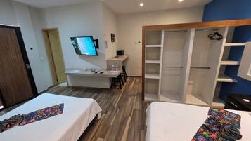 Quarto de hotel com duas camas, uma secretária com computador, televisão e guarda-roupa.