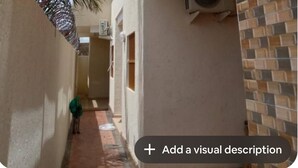 A narrow corridor with a tiled wall on one side and a palm tree on the other. - Cozy 1-bedroom apartment in beautiful Lomé with AC and internet. (Lomé)