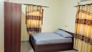 A bedroom with a single bed, curtains, a wardrobe, and an air conditioning unit. - Cozy 1-bedroom apartment in beautiful Lomé with AC and internet. (Lomé)