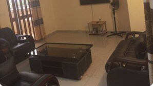 A living room with a flat-screen TV, a glass-top coffee table, a sofa, and a chair. - Cozy 1-bedroom apartment in beautiful Lomé with AC and internet. (Lomé)