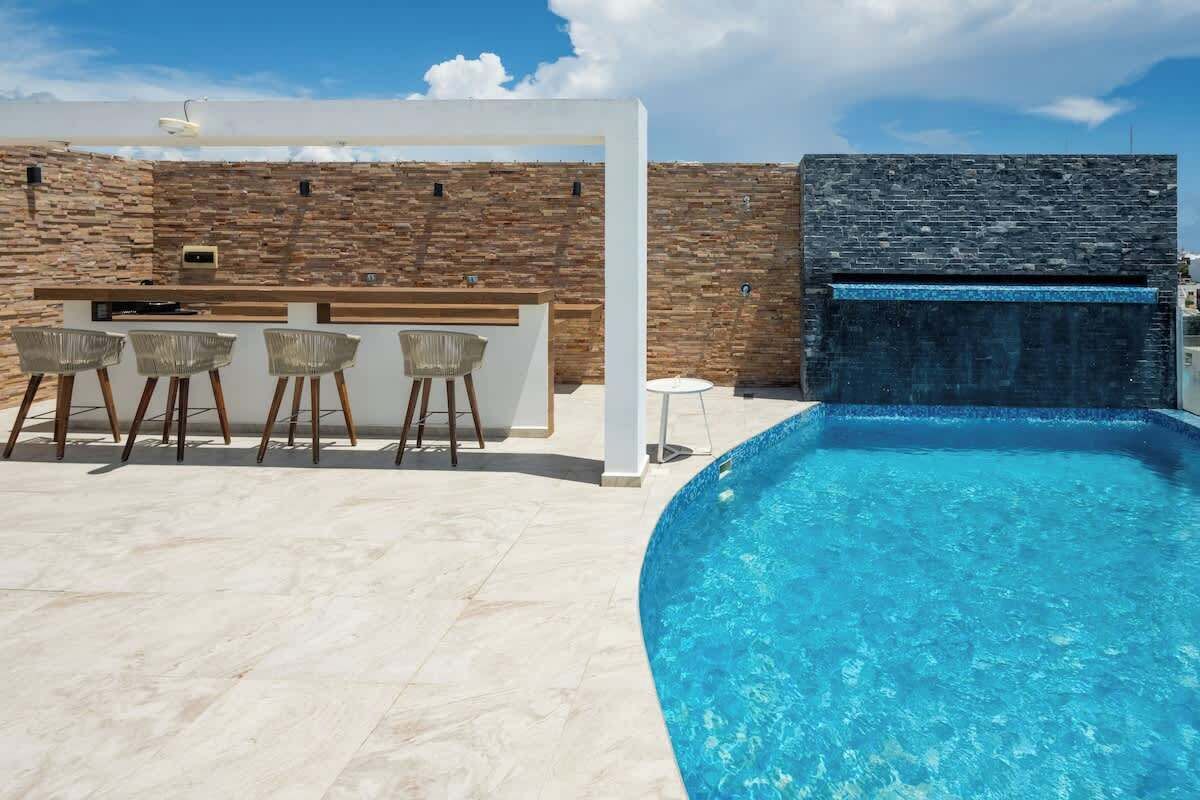 A pool area with a stone wall, a bar with stools, and a small table.