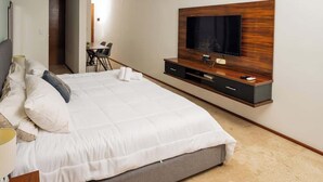Ein modernes Schlafzimmer mit einem großen Bett, einem an der Wand montierten Fernseher und einem kleinen Schreibtisch mit Stuhl.