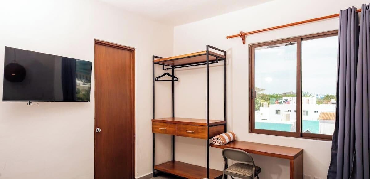 A room with a bunk bed, a desk, a chair, a TV, and a window with curtains.