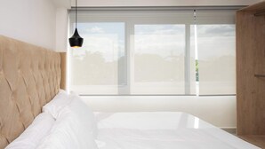 A modern bedroom with a large bed, a wooden headboard, and a large window with blinds. - Modern Apartment Pool, BBQ, and Prime Location (Cancún)