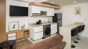 A modern kitchen with a microwave, sink, and refrigerator. There is a bar area with stools and a television mounted on the wall. - Modern Apartment Pool, BBQ, and Prime Location (Cancún)