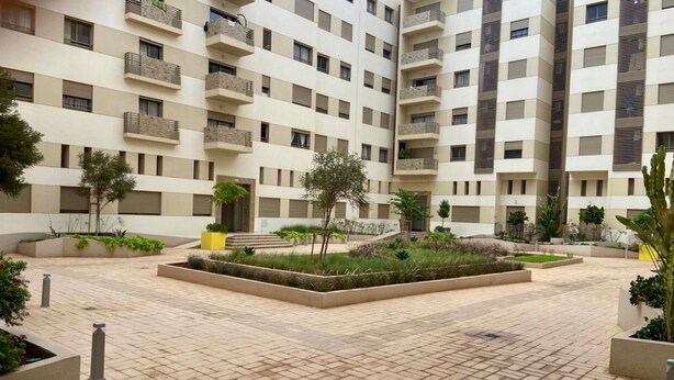 Un edificio residencial de varios pisos con balcones, un patio central con macetas y un pavimento de baldosas.