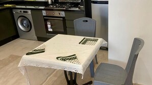 Una mesa de comedor con mantel de encaje, dos sillas, una lavadora y una estufa al fondo.