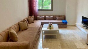 Una sala de estar con un sofá color beige, una mesa de centro blanca y un televisor sobre un mueble.