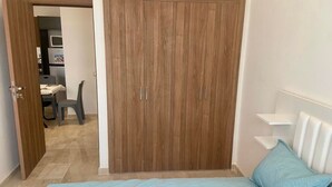 Un dormitorio con cama, armario y un pequeño escritorio con silla.